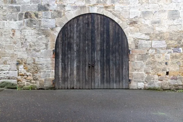 Antigua puerta de patio de madera de dos hojas en un muro de piedra de cantera