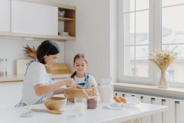 Madre e hija comparten un momento encantador haciendo masa juntas en una cocina iluminada por el sol.